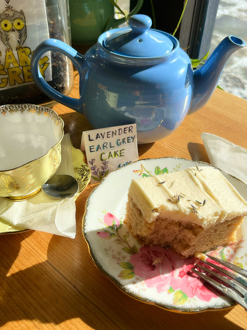 Blue teapot, cup of tea, and slice of lavender earl grey cake on a wooden table.