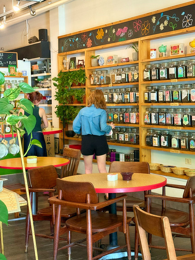 People inside of teastore with wooden chairs and a wall of jars.