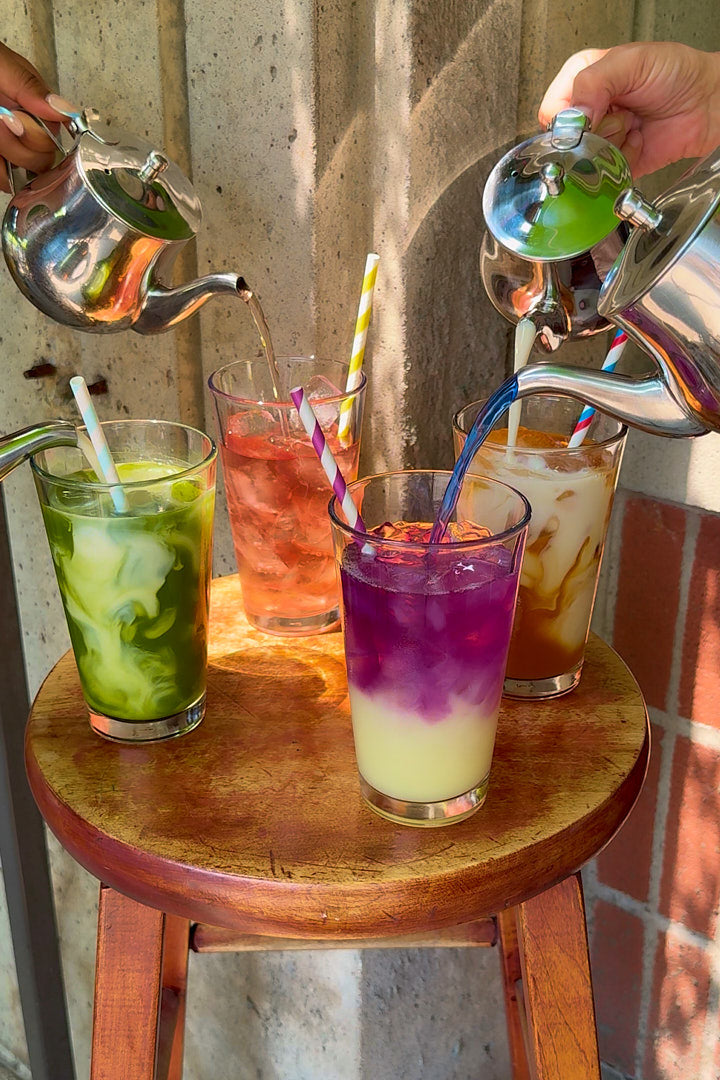 People pouring colorful drinks into glasses on a wooden stool.