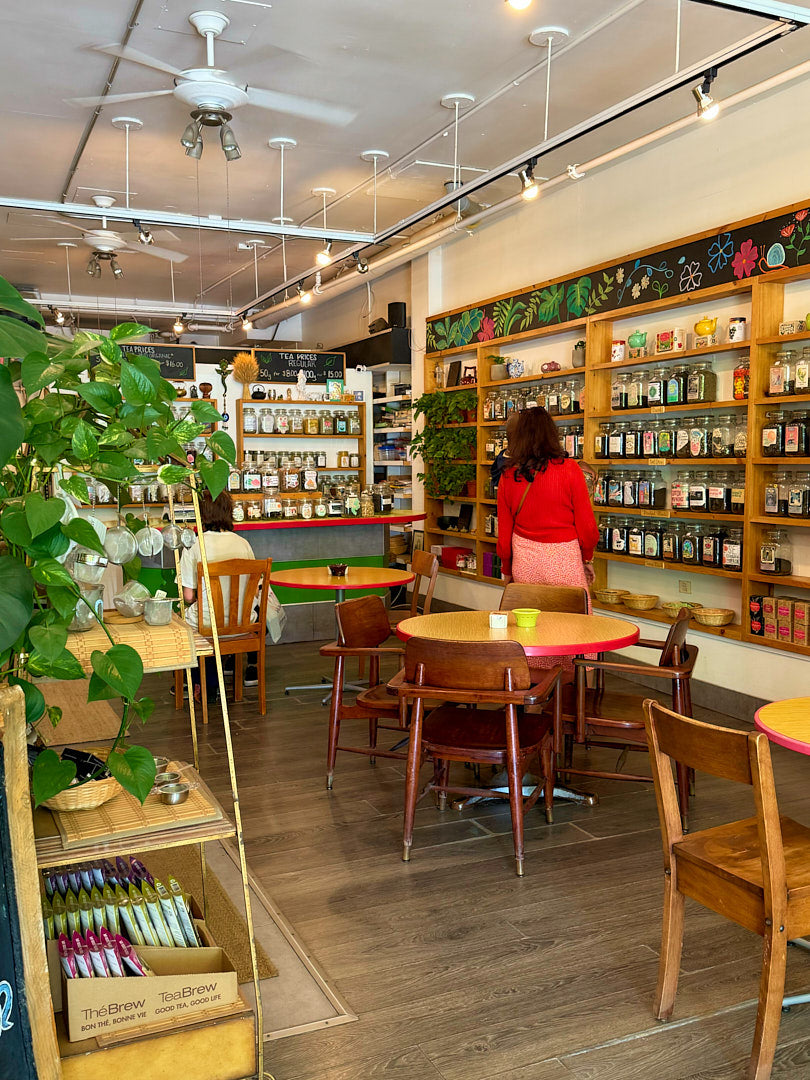 Interior of teastore with wooden furniture, shelves stocked with products, and a person in a red shirt.