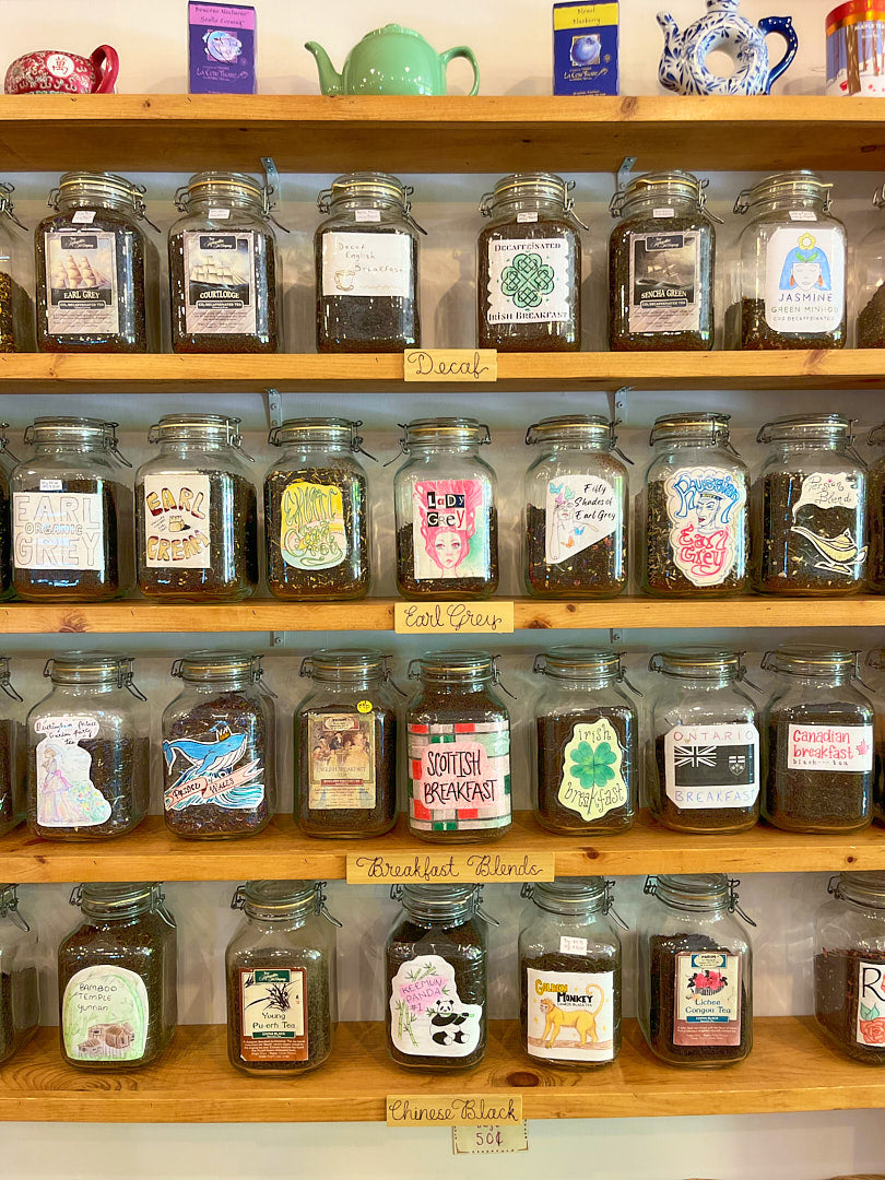 Shelves with glass jars labeled with various types of tea on a wooden shelf.