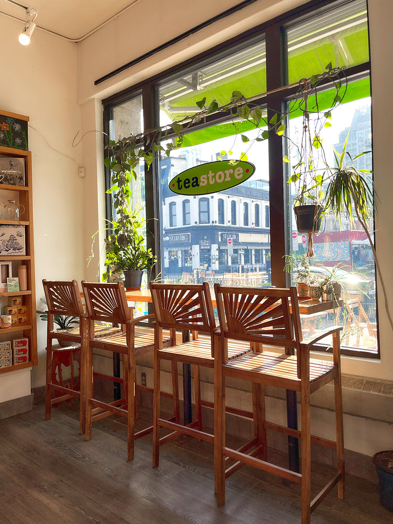 Dining area with wooden chairs and tables near a large window with 'Tea Store' sign.