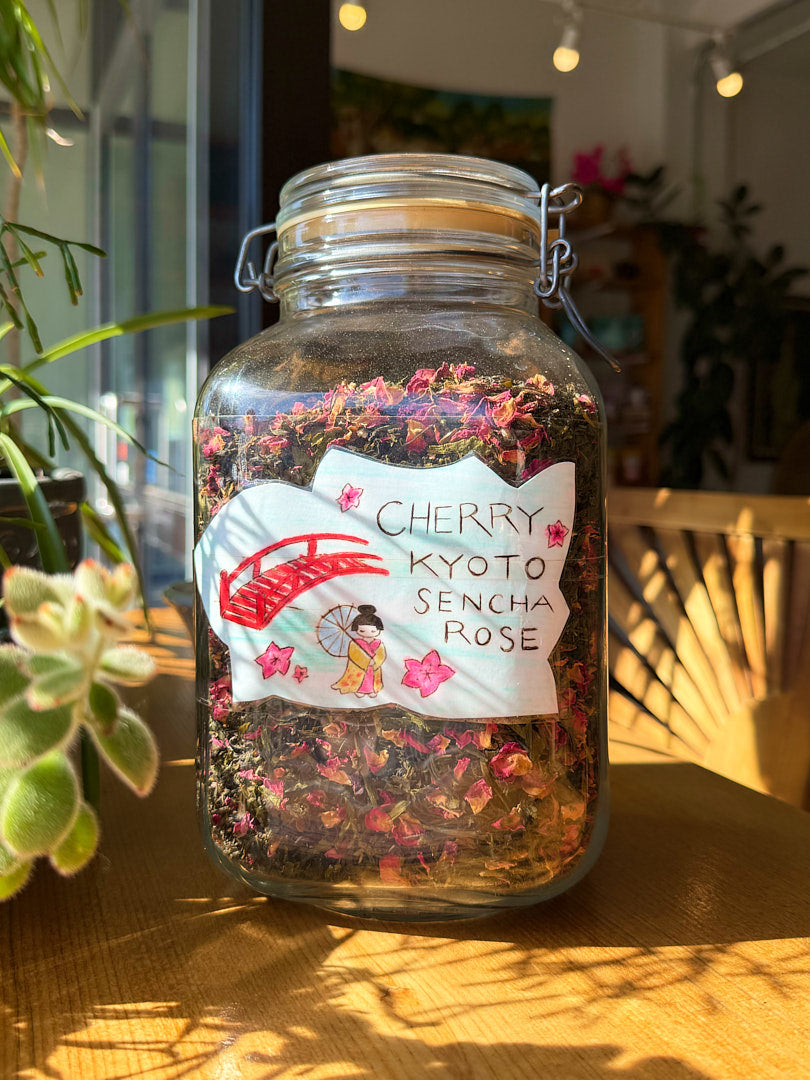 Glass jar with cherry Kyoto Sencha Rose tea on a wooden surface with plants in the background