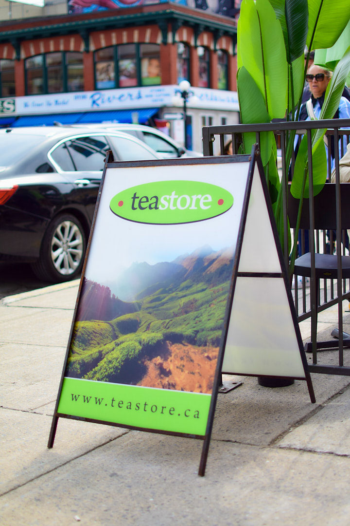 Outdoor sign for Teastore on a sidewalk with a scenic background